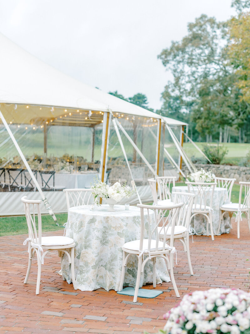 Outdoor reception tables with white chairs, floral tablecloths, and floral centerpieces