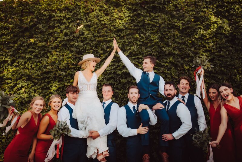 A bride and groom being held up by the groomsmen while they give each other a high five.