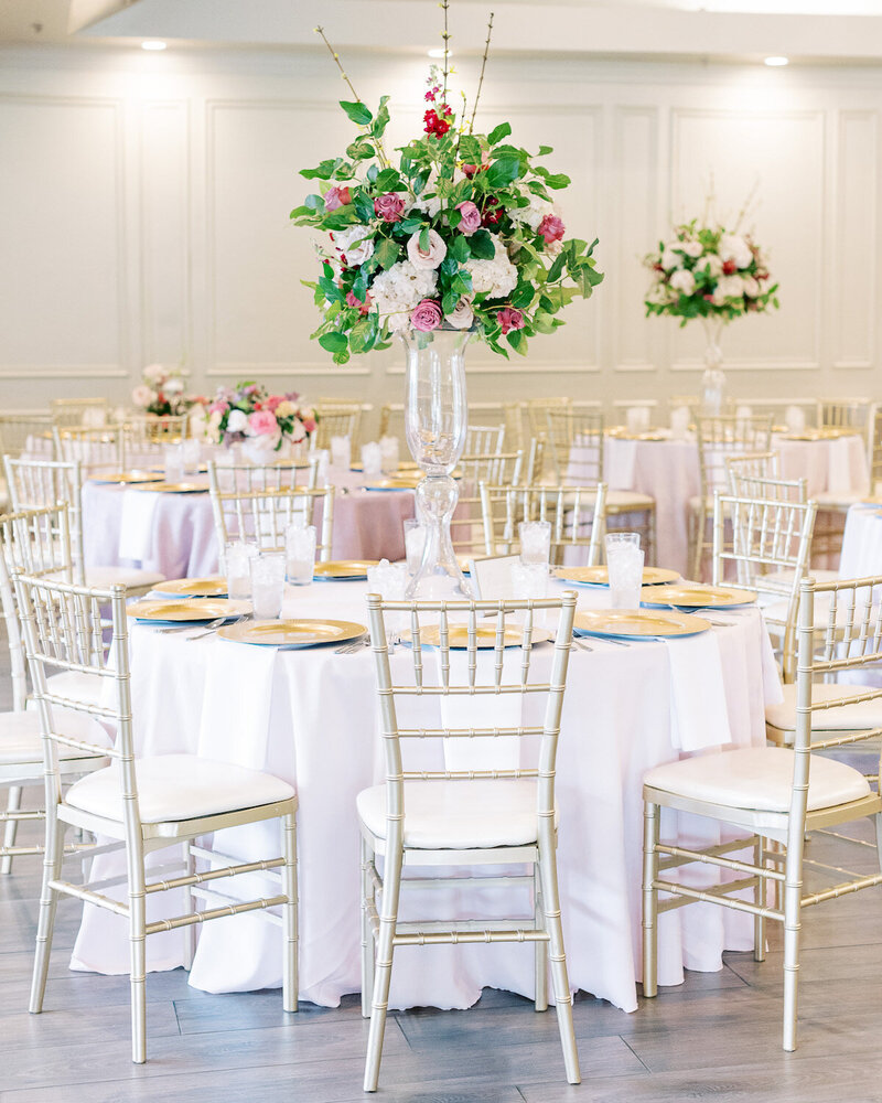 A room of tables with tall wedding floral arrangements