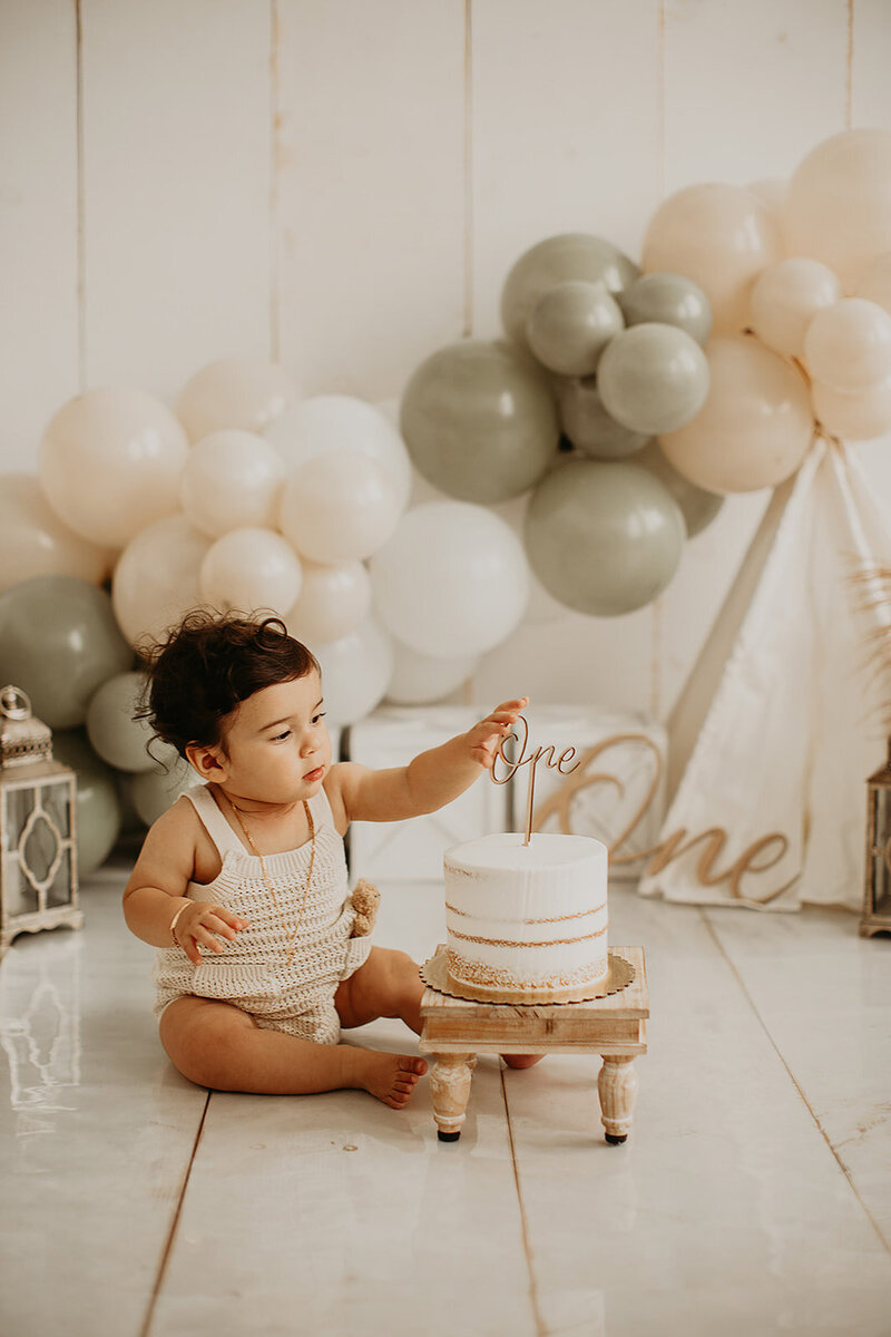 Child with a cake against a backdrop of balloons in a photo studio.