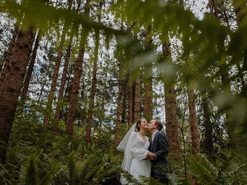 Groom kissing bride's cheek in a forest