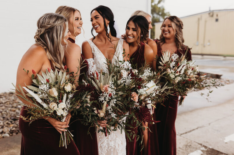 Wedding session photo of bride and bridesmaids holding bouquets smiling at each other