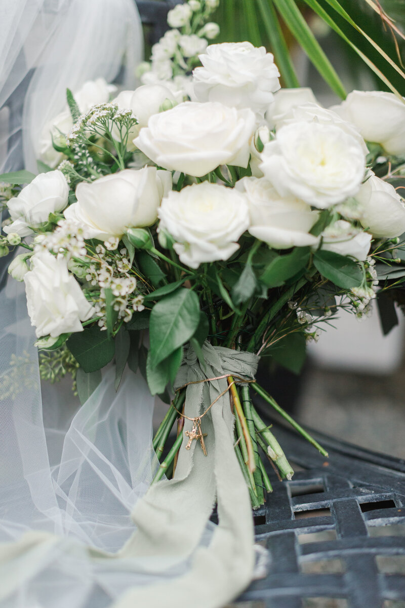 white wedding bouquet with a cross necklace tied to it