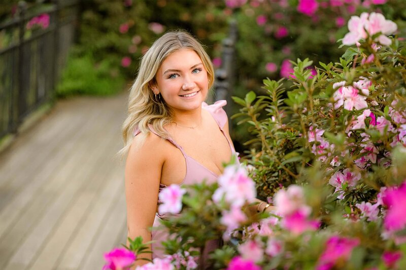 charlotte graduate is wearing a pink dress standing on a bridge with pink flowers around her