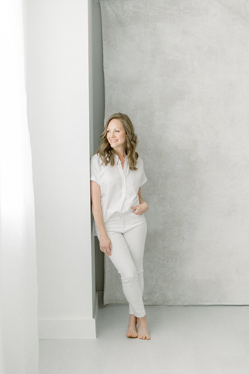 Photo of an in studio professional headshot taken of a Dallas business woman wearing a white shirt and pants as she looks out of the window and poses for her professional headshots.