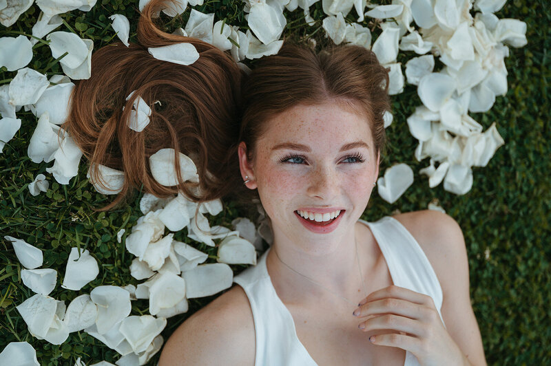 redheaded girl with freckles lays in a pedal of white flowers