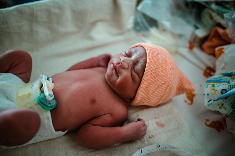 Newborn baby lying in crib wearing an orange hat