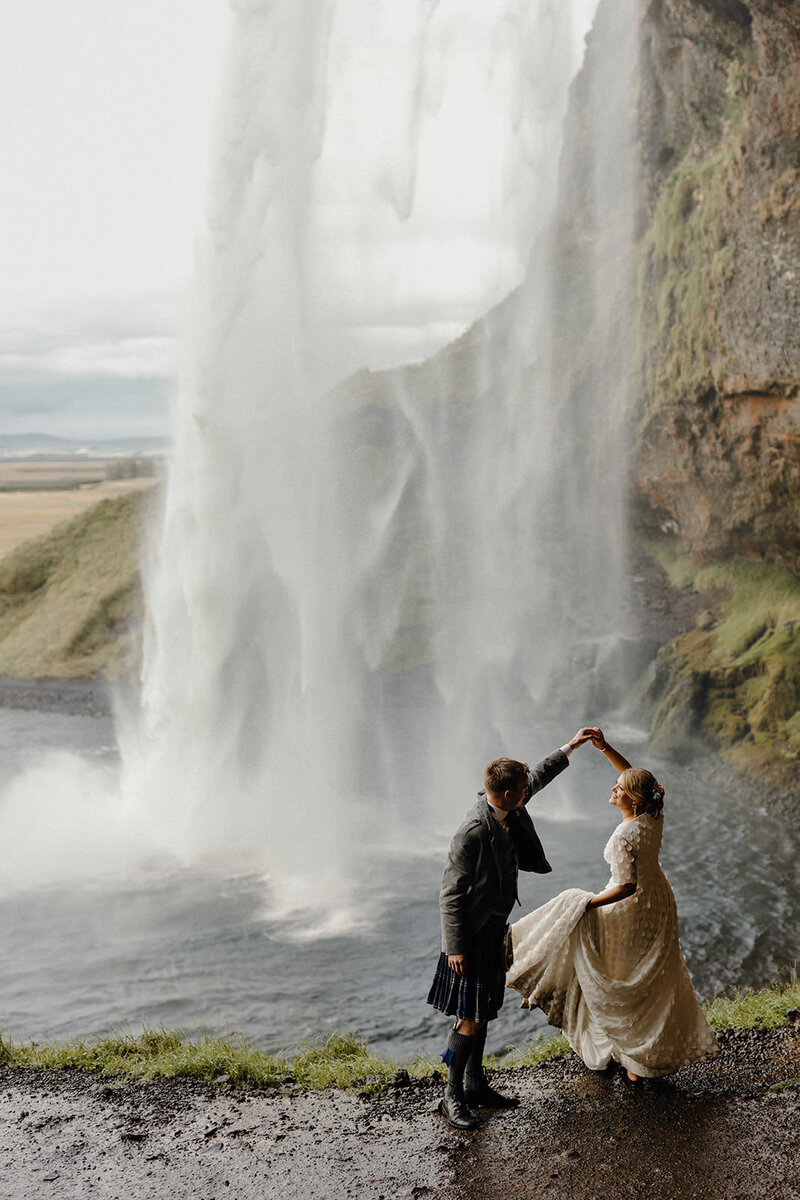 bride and groom dance beneath waterfall in Iceland
