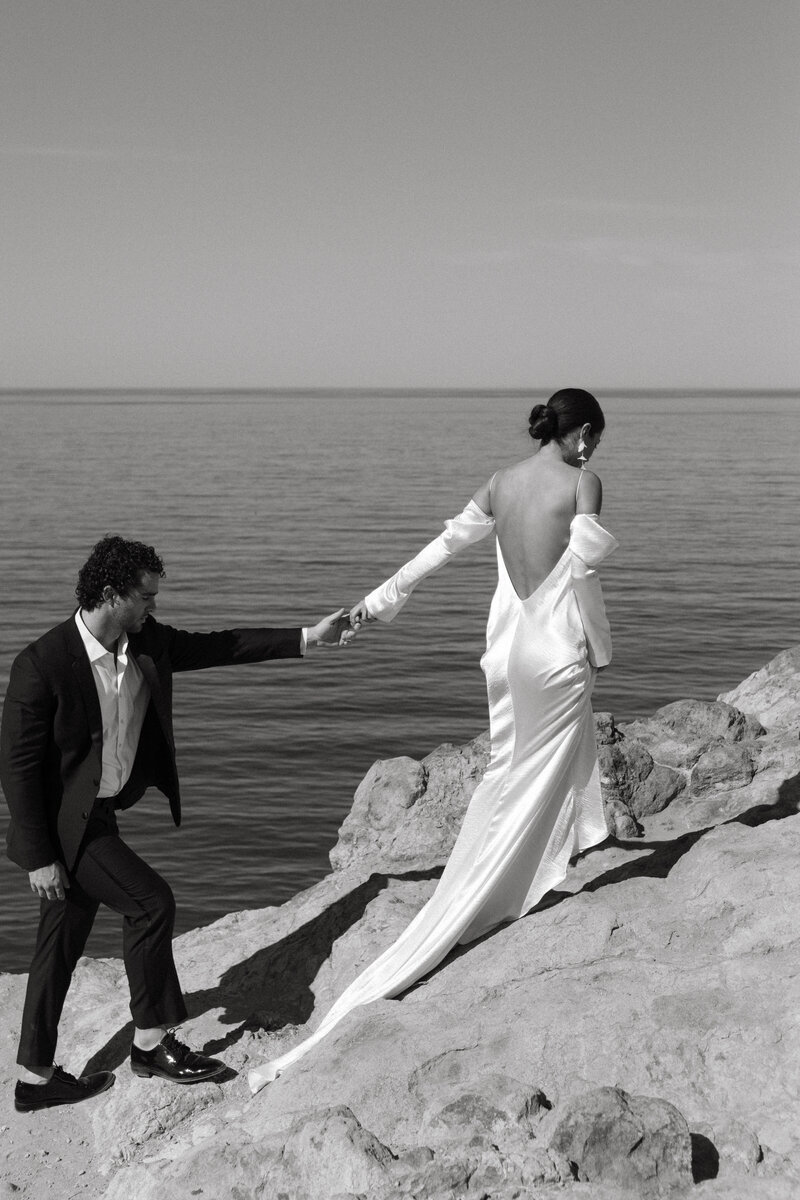 bride and groom holding hands on the cliffside next to the ocean