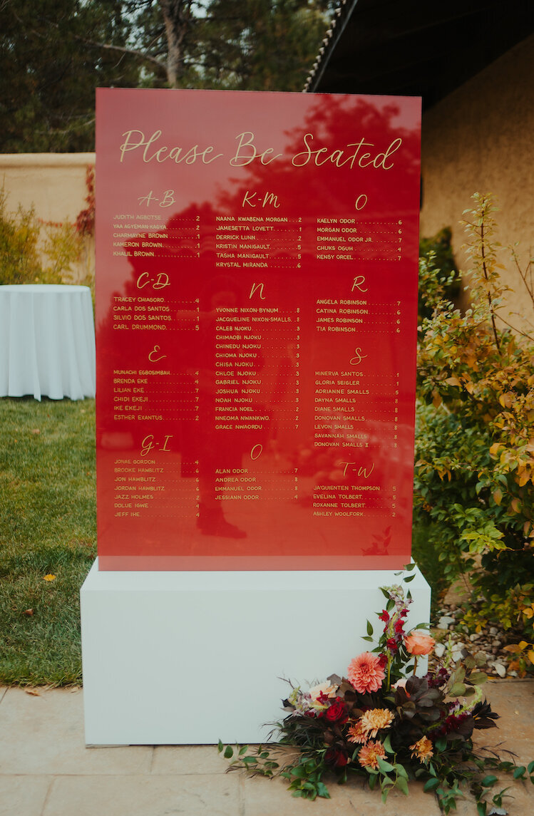 Maroon and gold calligraphy seating chart in a white stand for a fall wedding