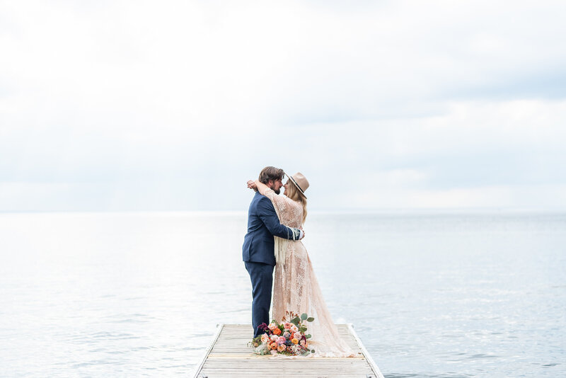 Bohemian bride and groom embrace at the end of a dock on their wedding day