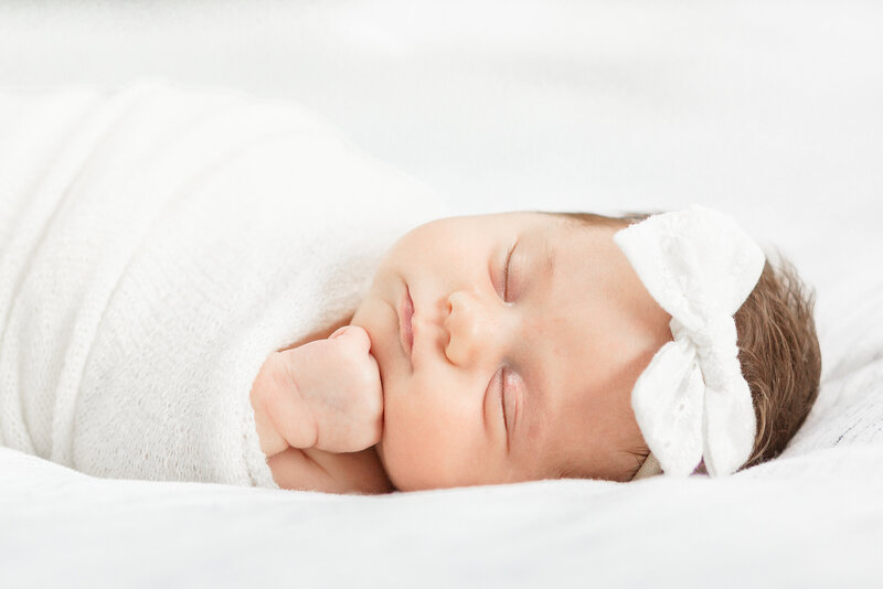 Ann Arbor Newborn Photographer takes photo of newborn baby girl on bed, swaddled