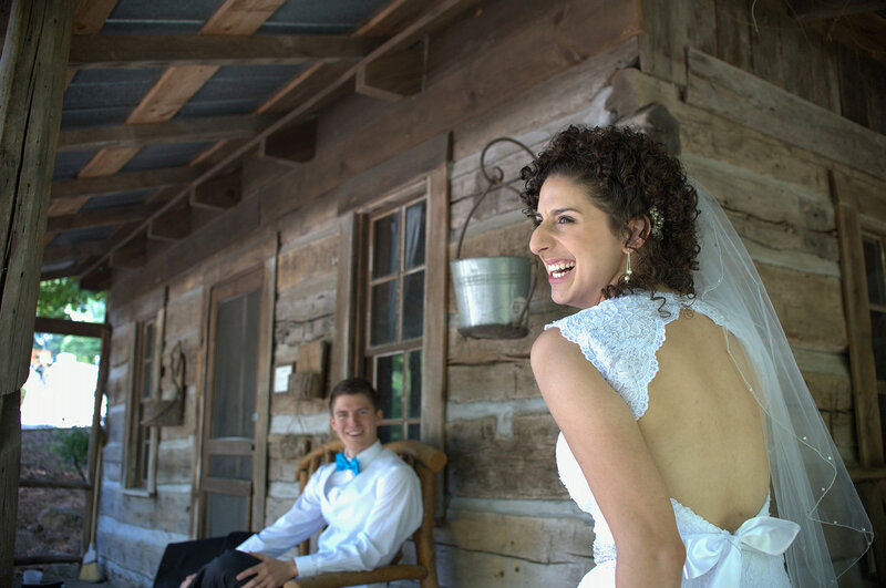 Bride in open backed lace detail dress laughs with groom in background