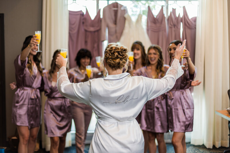 Bride and bridesmaids toasting each other with glasses of mimosas while getting ready