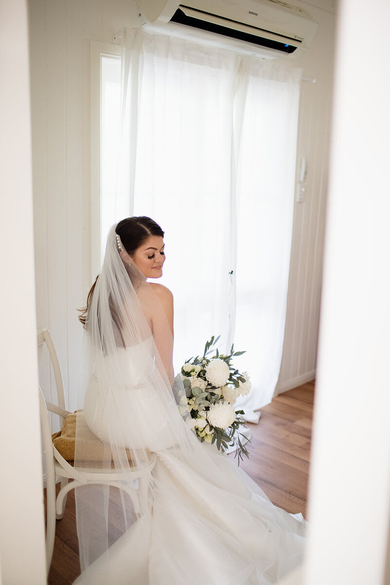 Bride poses and sits on with her long wedding veil and a bouquet in her hand