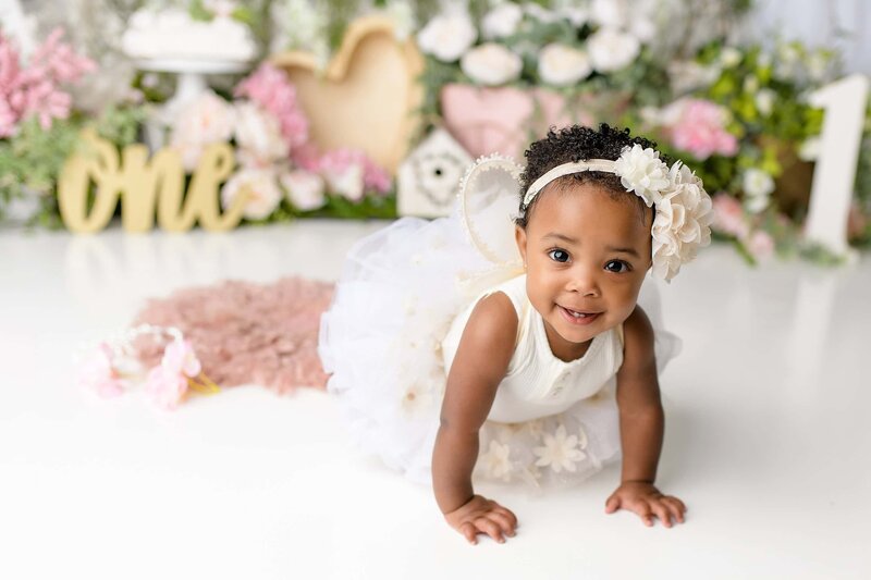 little one year old girl dressed in cream crawling and smiling in her studio cake smash set up