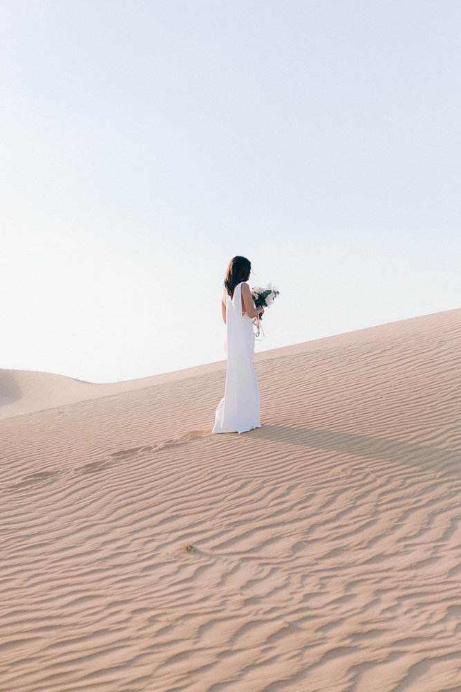 bride walking in the sand during sunset in the desert of dubai for her wedding