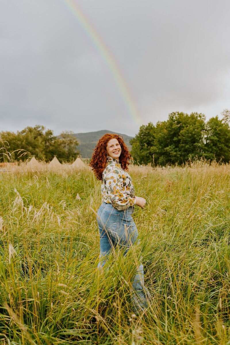 Leanna stands in a field with a rainbow in the background