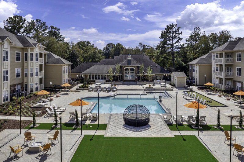Commercial apartment pool design. Featuring a variety of bold seating, beautiful landscape design, string lights, and other amenities. Design by Gracious Home Interiors, luxury interior designer in Waxhaw, North Carolina and across the east coast.