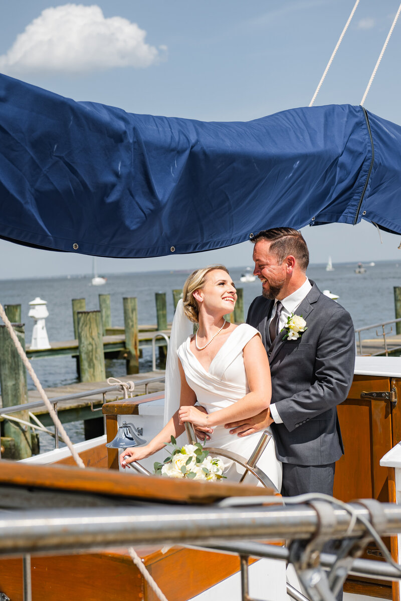 A bride and groom standing together steering a boat.