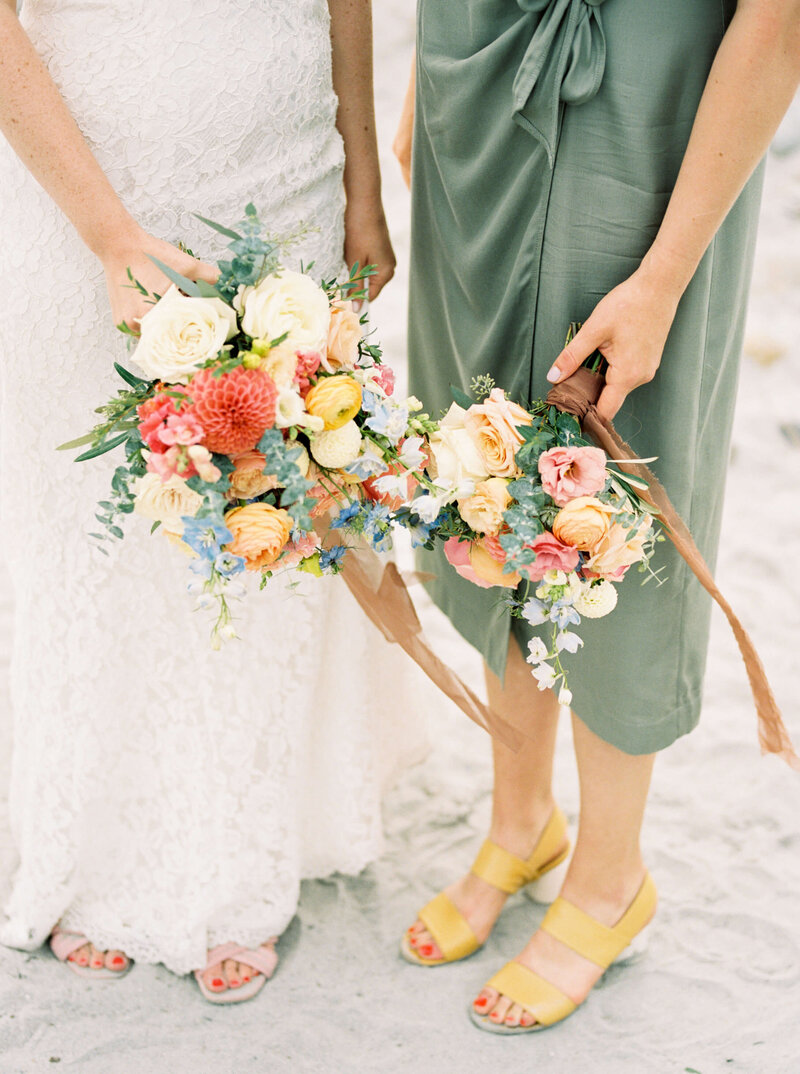 Bride with bridesmaid in olive dress holding bouquets of florals