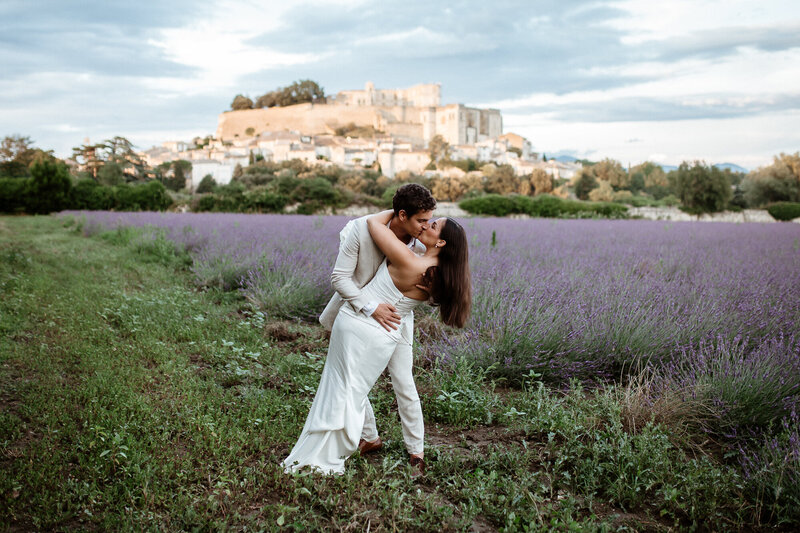 Couple kissing in Grignan with a castle andlavender fields in thebackground