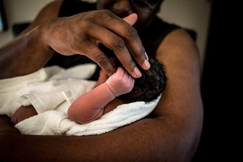 Black woman holding newborn baby and stroking hand