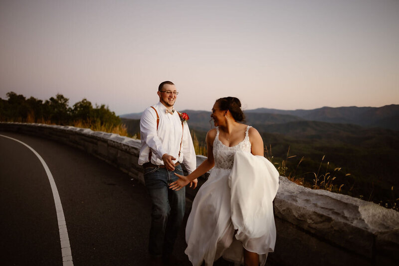 Foothills Parkway elopement in the Smoky Mountains with groom running after his bride down the parkway while the bride turns to reach for the grooms hand as they elope to Gatlinburg 