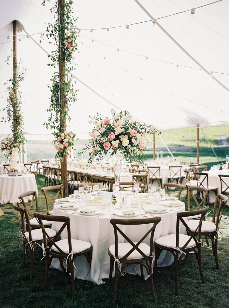 testimonial photo, empty tented reception featuring tall bouquets of pink flowers, foliage and pink flowers decorate wooden tent poles