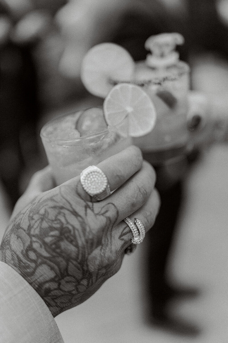 Tattooed hand holding a cocktail with lime garnish during a stylish reception in Los Angeles captured in documentary style