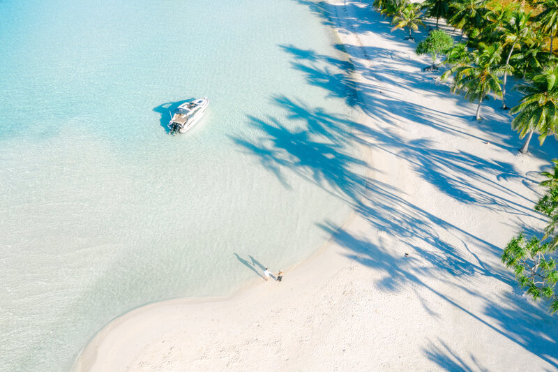 Aerial view on a private motu, couple walking on the beach near their private boat