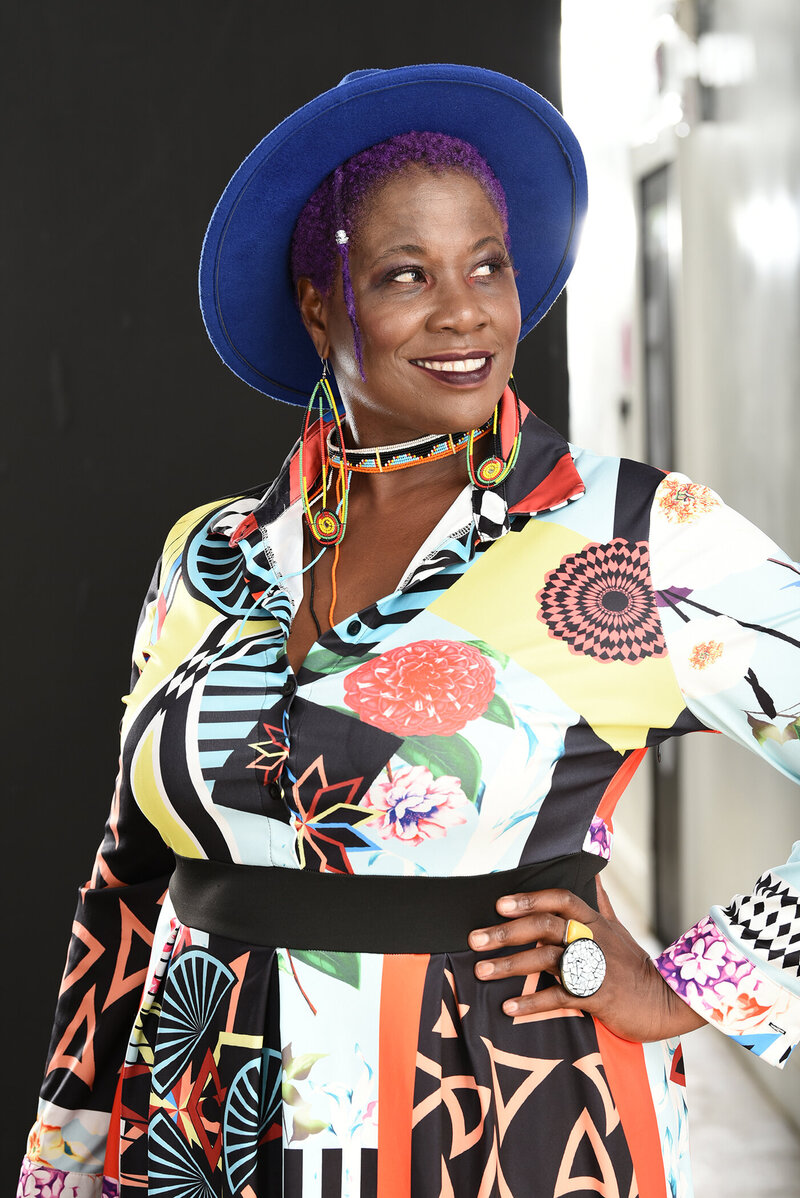Photo of Lisa Zunzanyika black woman wearing a blue hat and colorful abstract patterned dress