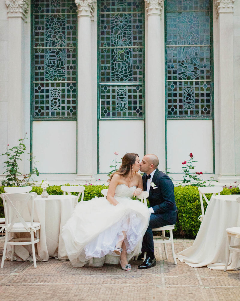 Bride + Groom sit at a table and share a kiss