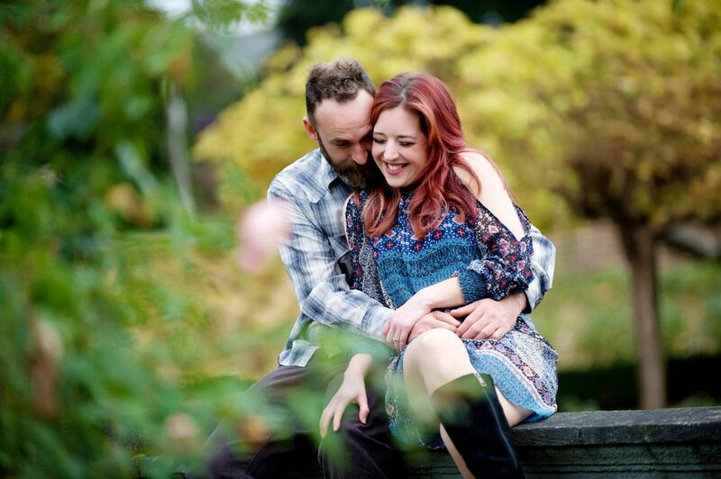 a man and a woman with red hair hug while sitting on a wall during their engagement photos at peninsula park in the fall