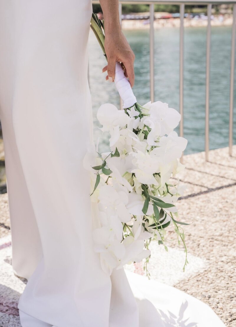 Bride holding white floral bouquet on pier.