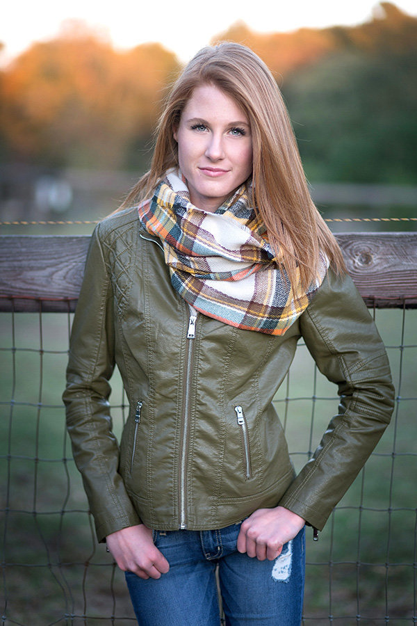 High school senior girl smiles in green leather jacket and scarf for senior portraits