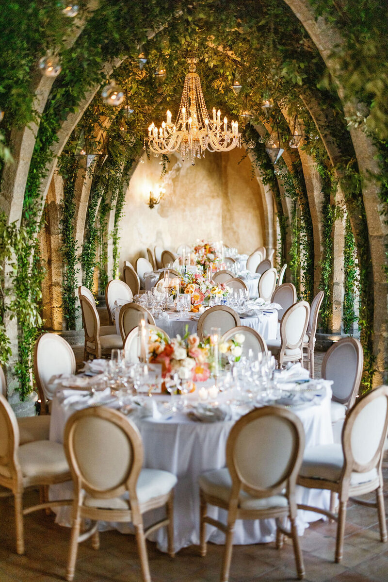 Wedding reception tables set up in an outdoor arched corridor overgrown with ivy