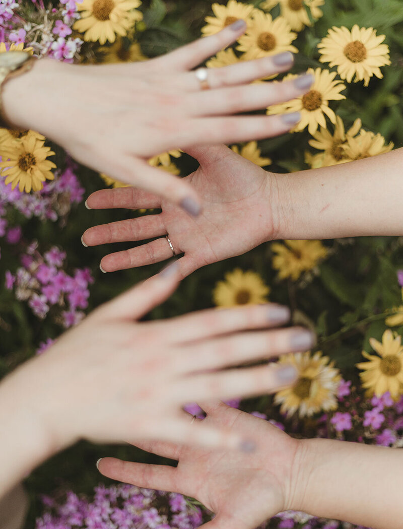 hands over each other with yellow and purple flowers underneath