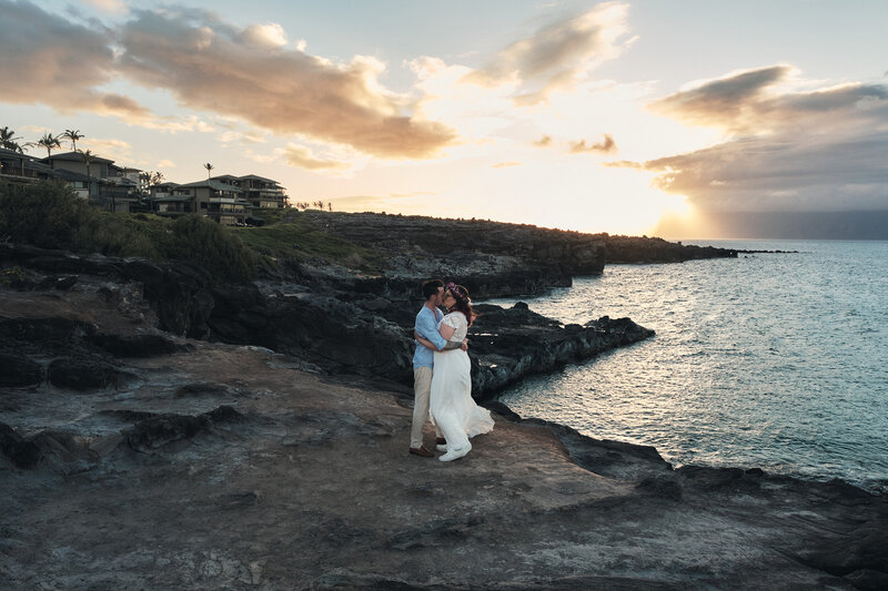 Eloping couple kisses among the rocky coastline at sunset
