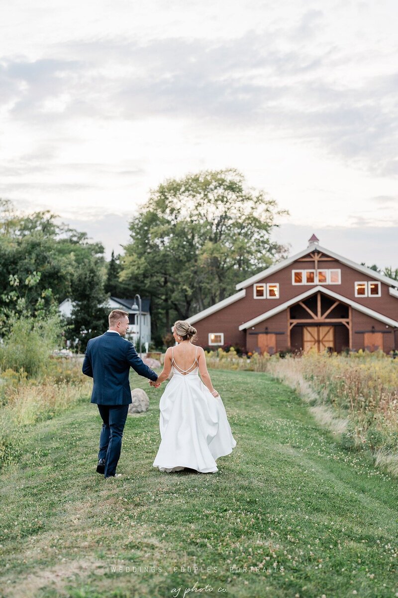 bride and groom walking hand in hand in the outdoor site at barnwood events, a wedding venue in madison, winconsin.