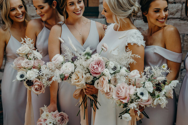 A group of 5 bridesmaids carry modern white and blush bouquets with no greenery in line with the bride at the industrial venue Airship37 in Toronto Canada