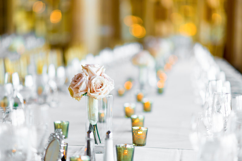 Small peach rose centerpiece atop a long table at a reception