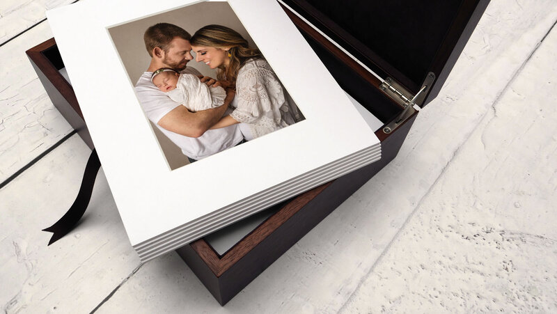 brown wooden keepsake display box with matted parent newborn images on top on white wood floor
