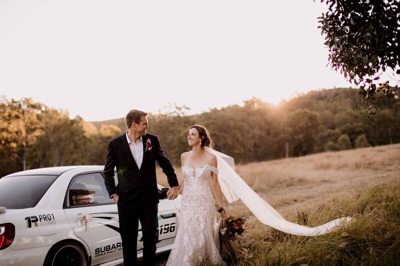 Bride and Groom holding hands with car at the back
