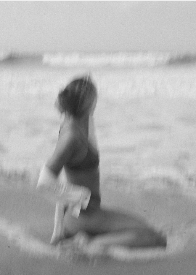 Black and white grainy film photography of a women sitting on the beach