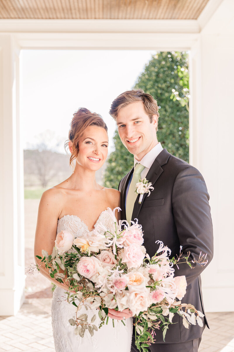 A brunette bride on her wedding day laughing with her husband while holding pastel pink flowers at Donovan Manor by JoLynn Photography