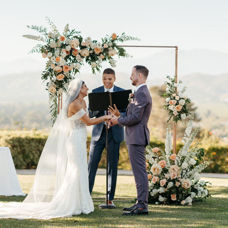 Large flower and greenery filled bouquets surround the bride and groom at the wedding arbor at the Spanish Hills Country Club in Camarillo, California.