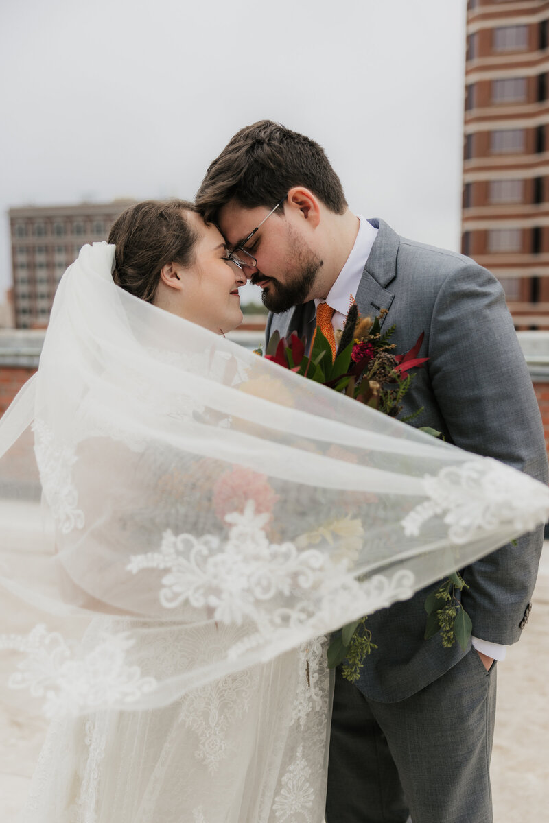 bride and groom touching foreheads while wrapped in veil