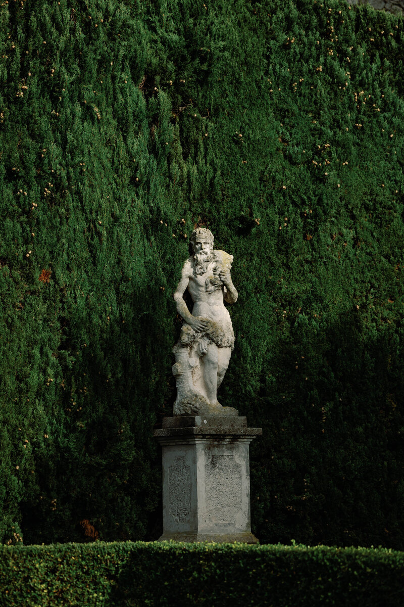 Engagement photo of couple embracing in the formal gardens at Philbrook Museum in Tulsa, Oklahoma surrounded by manicured hedges, cypress trees, and classic European architecture in black and white