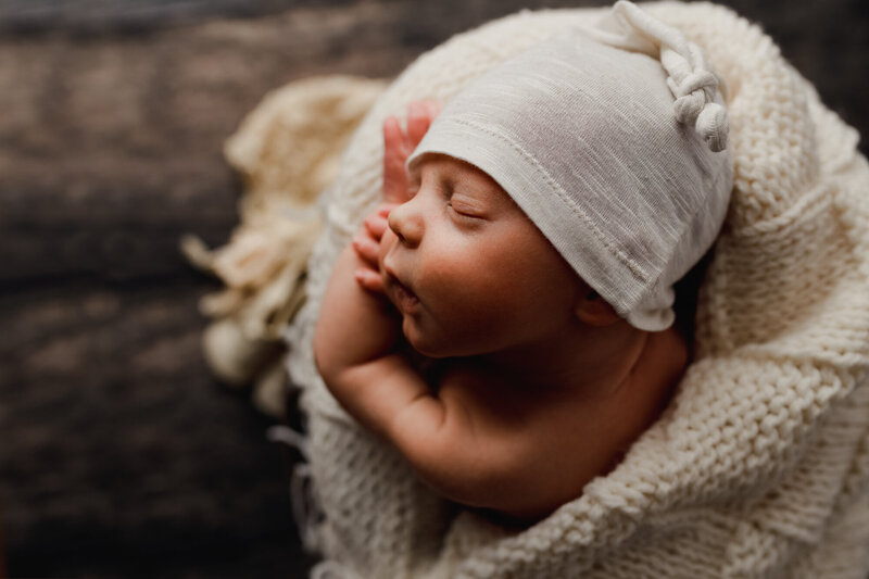 newborn baby sleeping in bucket with heirloom blanket and white hat